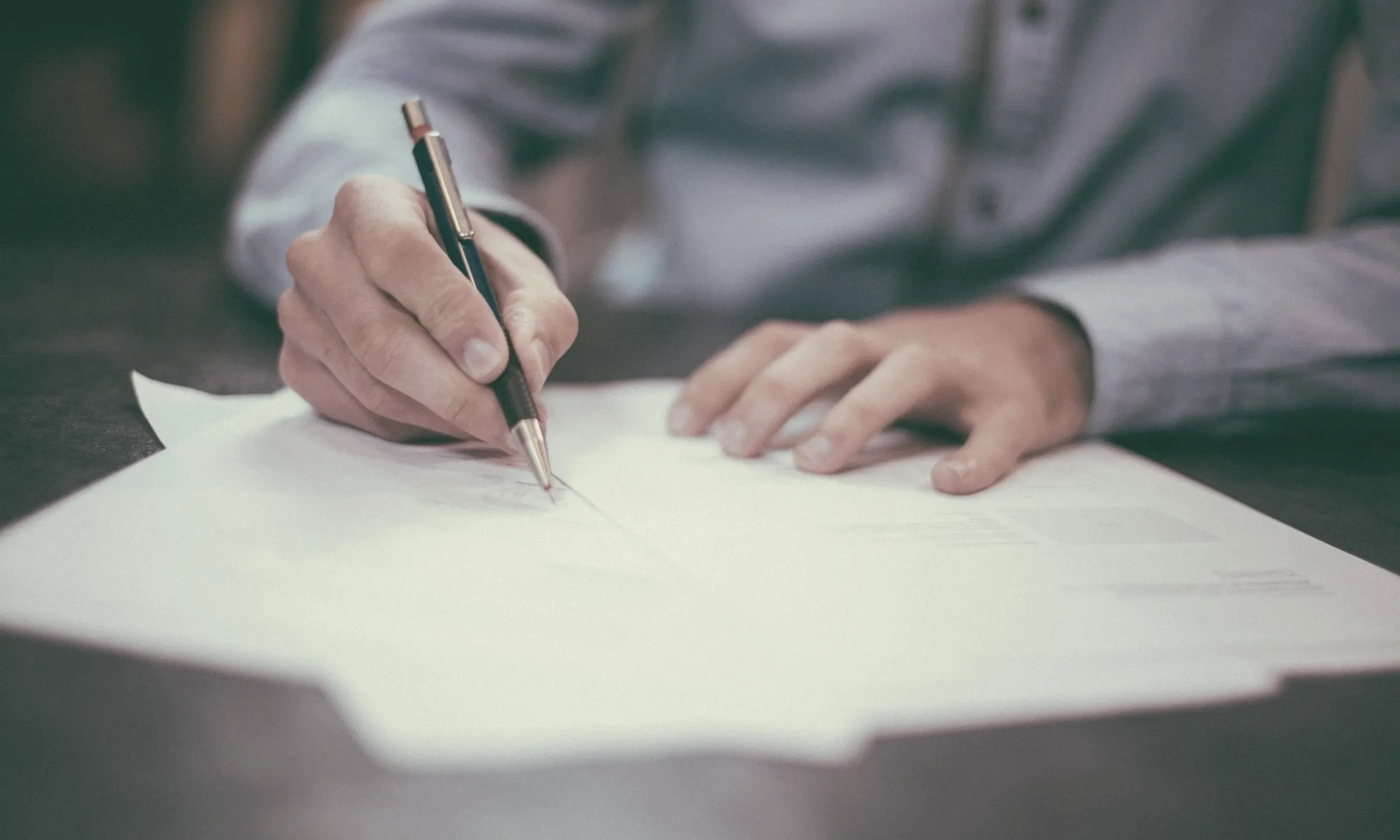 A hand signing documents with a pen