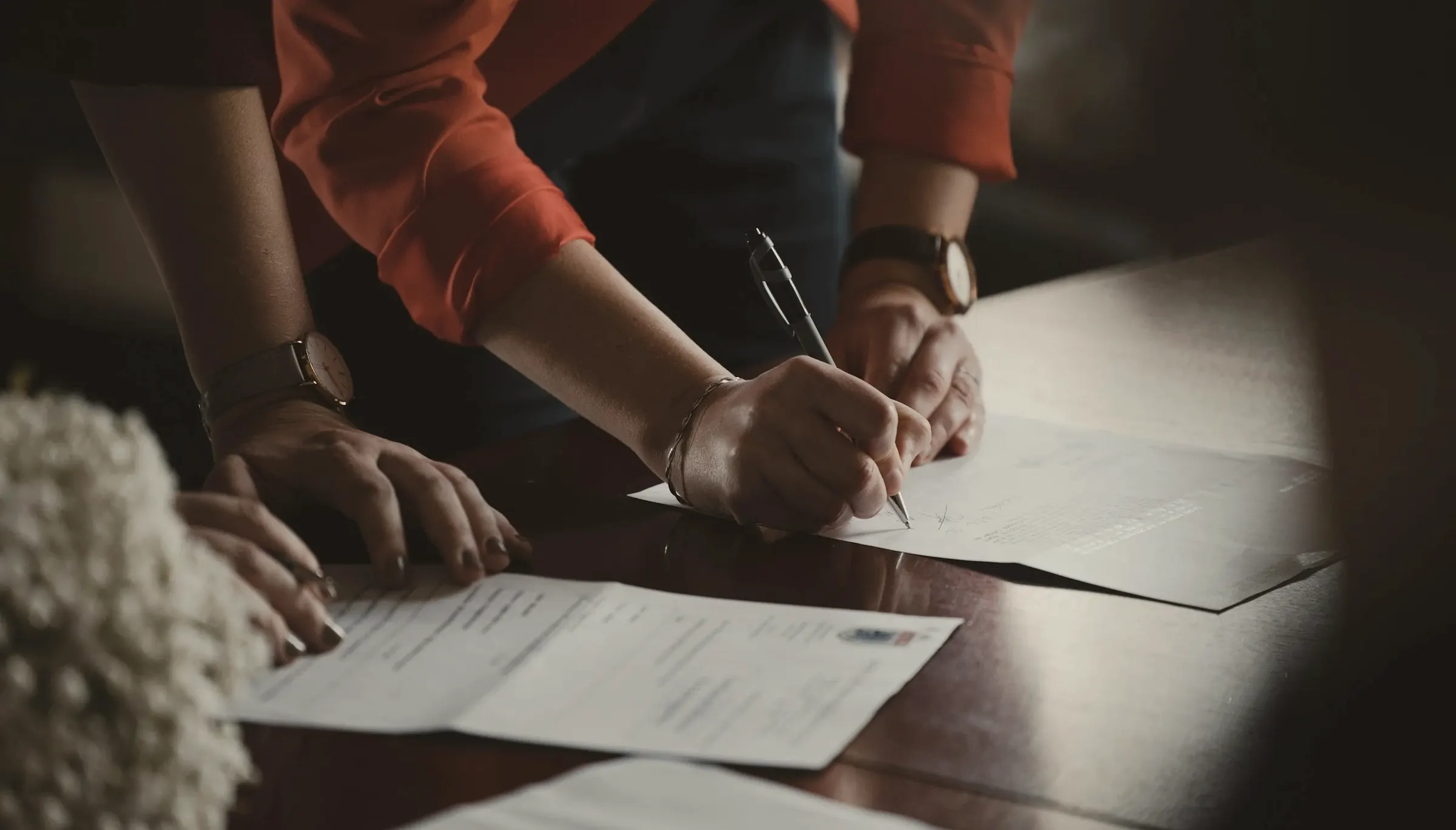 Two people leaning over a timber table reviewing and signing documents